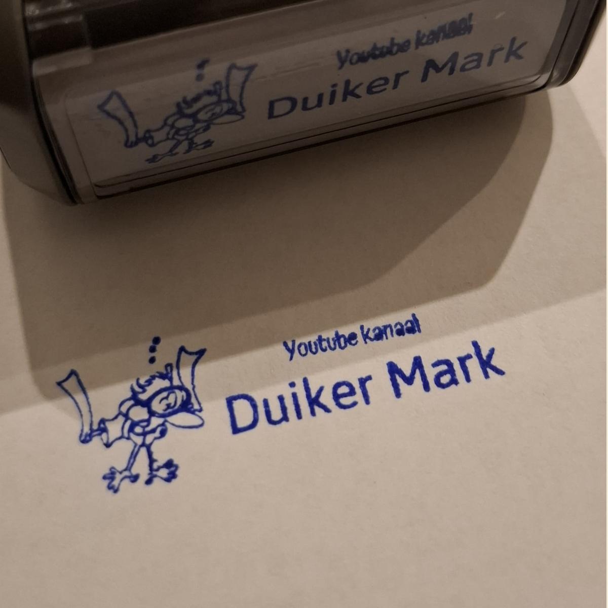 A self-inking stamp beside a fresh blue imprint of a cartoon diver and the words Duiker Mark.