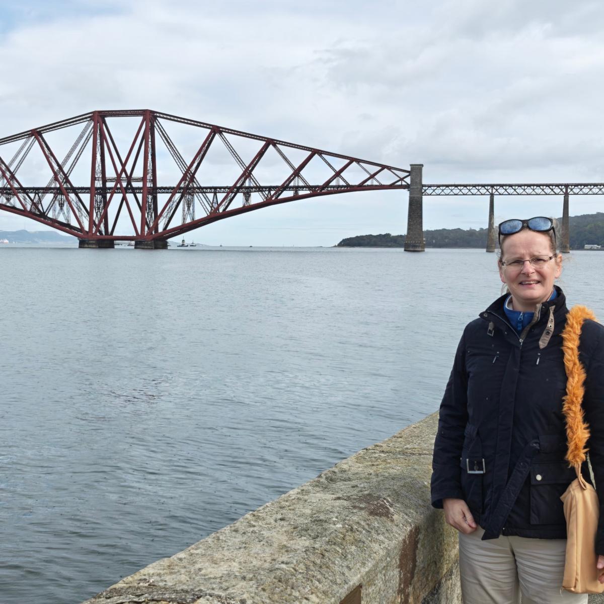 Daytime photo of the red cantilever Forth Bridge across grey water.