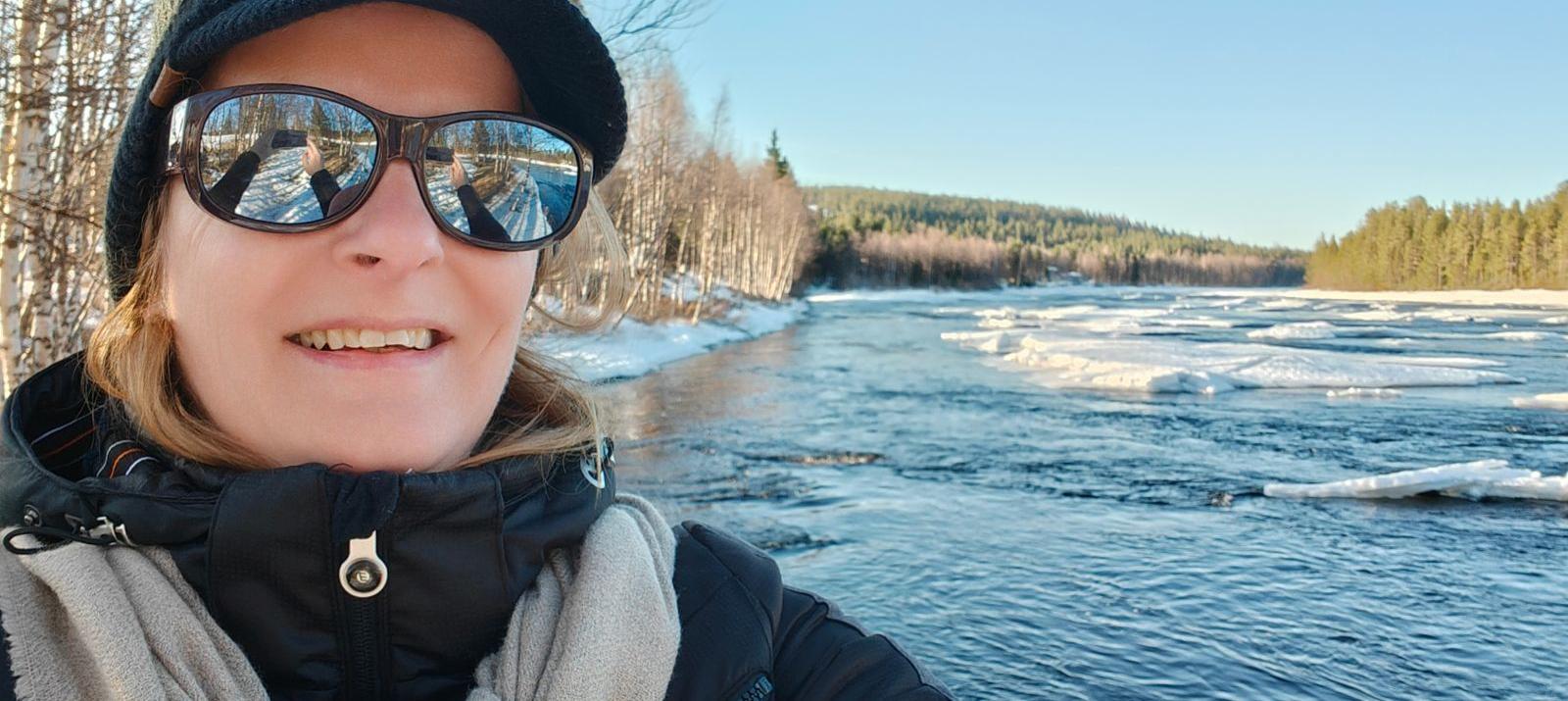 Els Bancken by the Ounasjoki river in Finnish Lapland in late April, open flowing water in the centre and drifting ice floes along the bank under a clear blue sky.