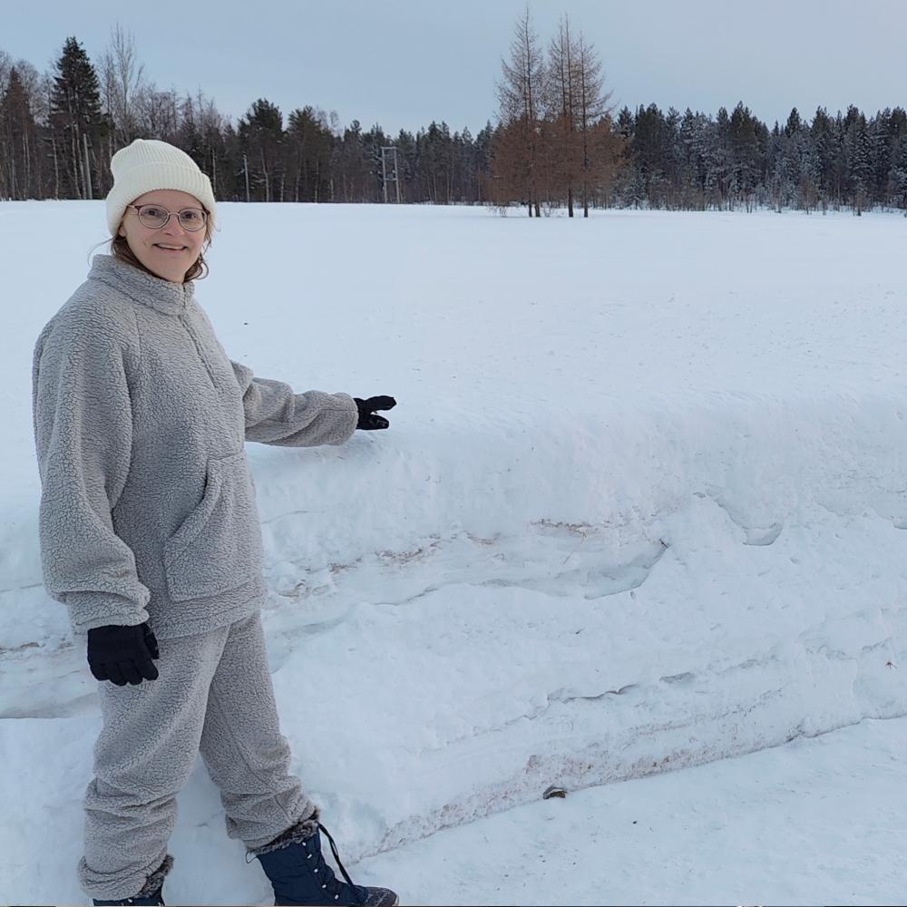 Els Bancken standing beside a chest-high snowbank in Tepasto, Finnish Lapland, showing the depth of the winter snow.