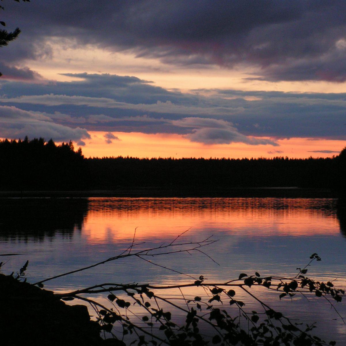A calm northern lake at dusk, the sky in soft bands of colour reflected in still water