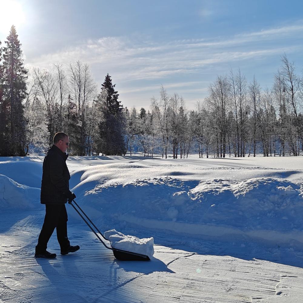 A person walking across a wide, sunlit snowfield in Finnish Lapland in late March, standing on top of a thick, firm snow crust.