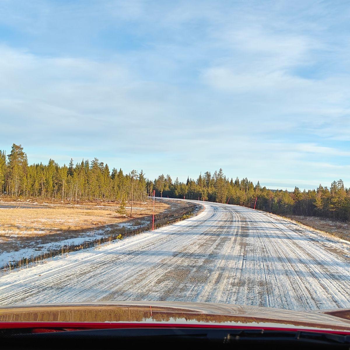 View through a car windscreen of a snow-dusted road in Finnish Lapland at the end of October, the season's first snow, with bare grass along the verge.