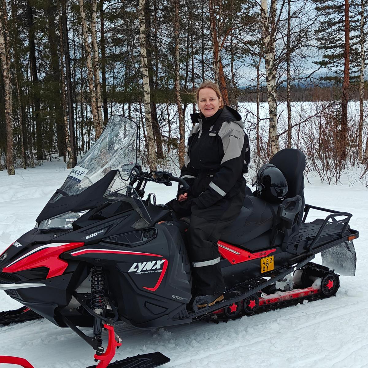 Me in a black thermal suit seated on a black and red snowmobile on a snowy trail in Finnish Lapland, ready for a guided snowmobile tour. Aurealis Creatief.