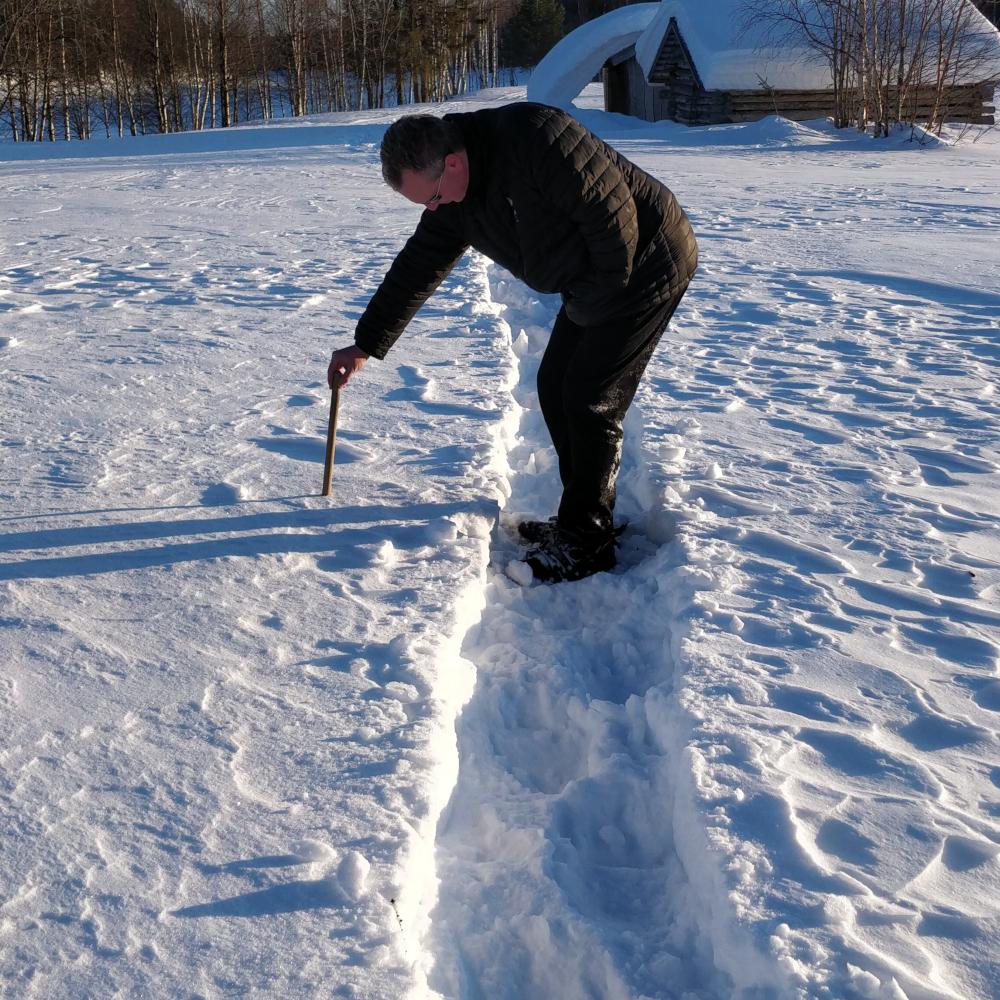 A person crouching and testing a thick snow crust in Lapland, the surface firm enough to stand on but still soft in places.